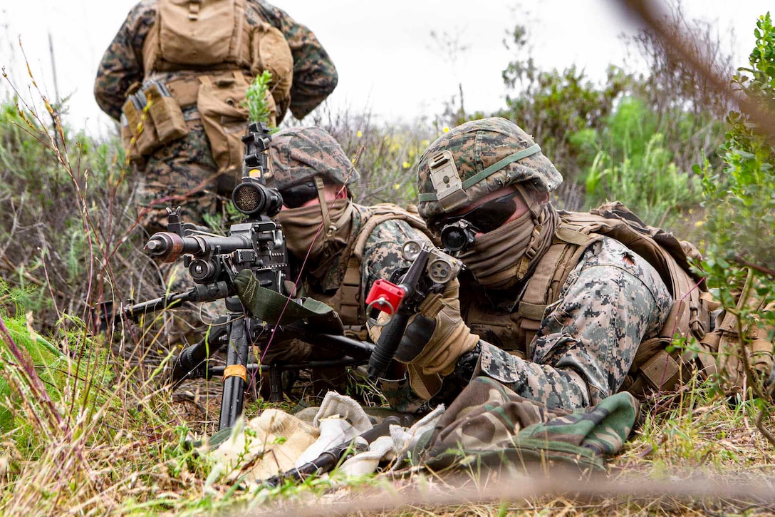 Two Marines lie on the ground pointing weapons.