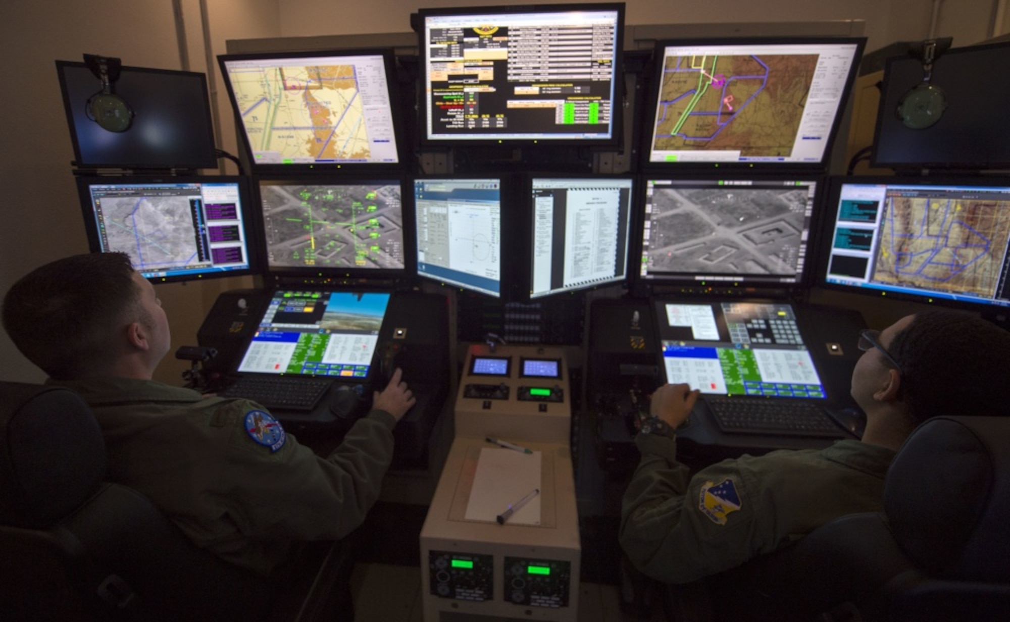 two Airmen sit in front of multiple monitors in dark room