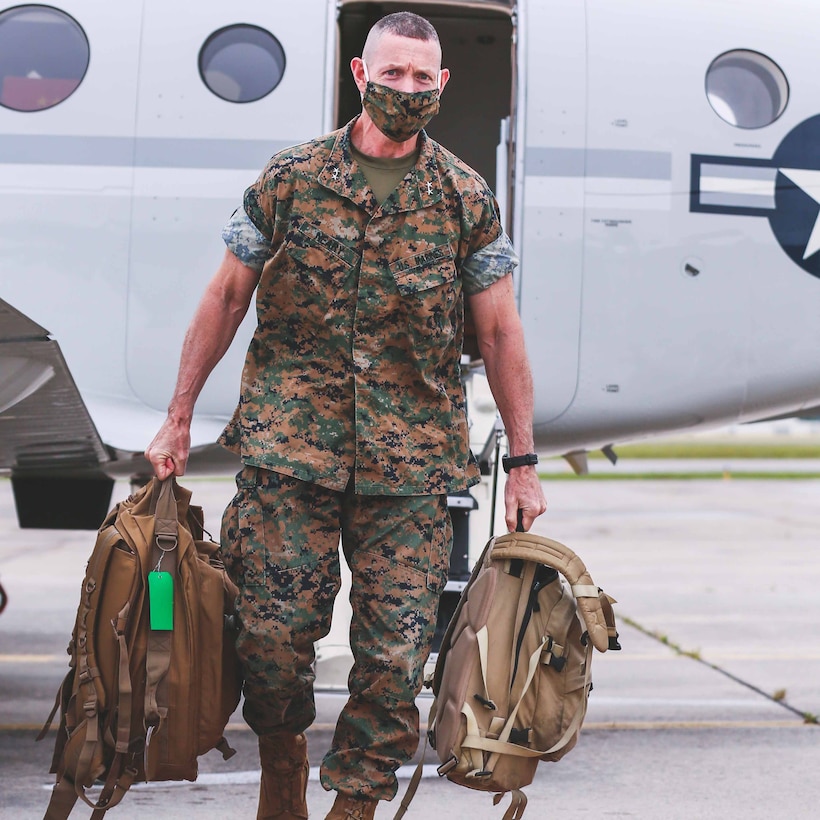 Marine Corps general wearing a face mask walks off a military aircraft.