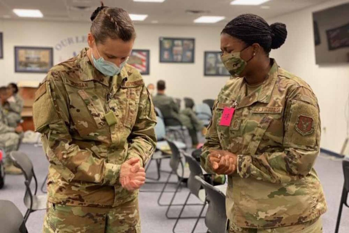 Two airmen wearing face masks fold their hands and bow their heads.