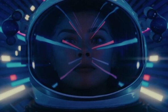A female astronaut looks forward surrounded by lights.