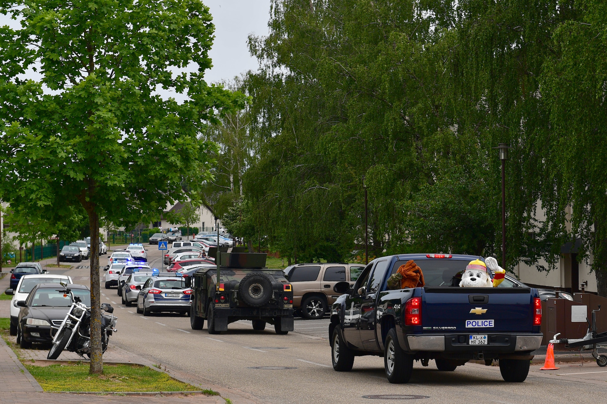 McGruff the Crime Dog and Sparky the Fire Dog sit in a truck bed and wave from the back of a convoy of first responder vehicles.