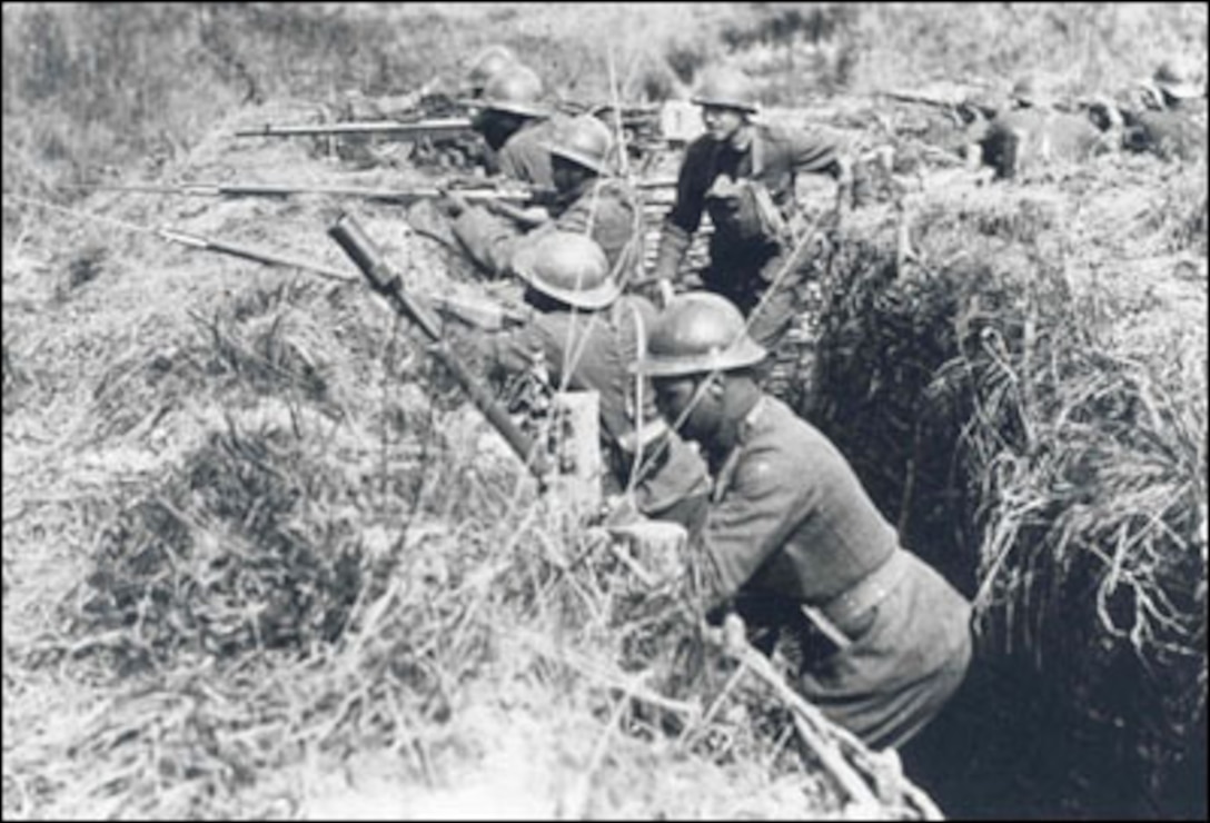Men standing in trenches aim rifles into the distance.