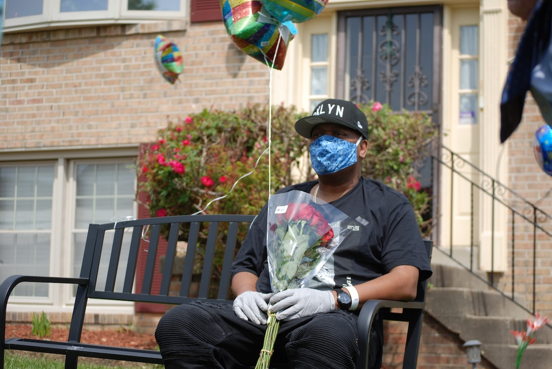 A man holding flowers and balloons sits on a bench.