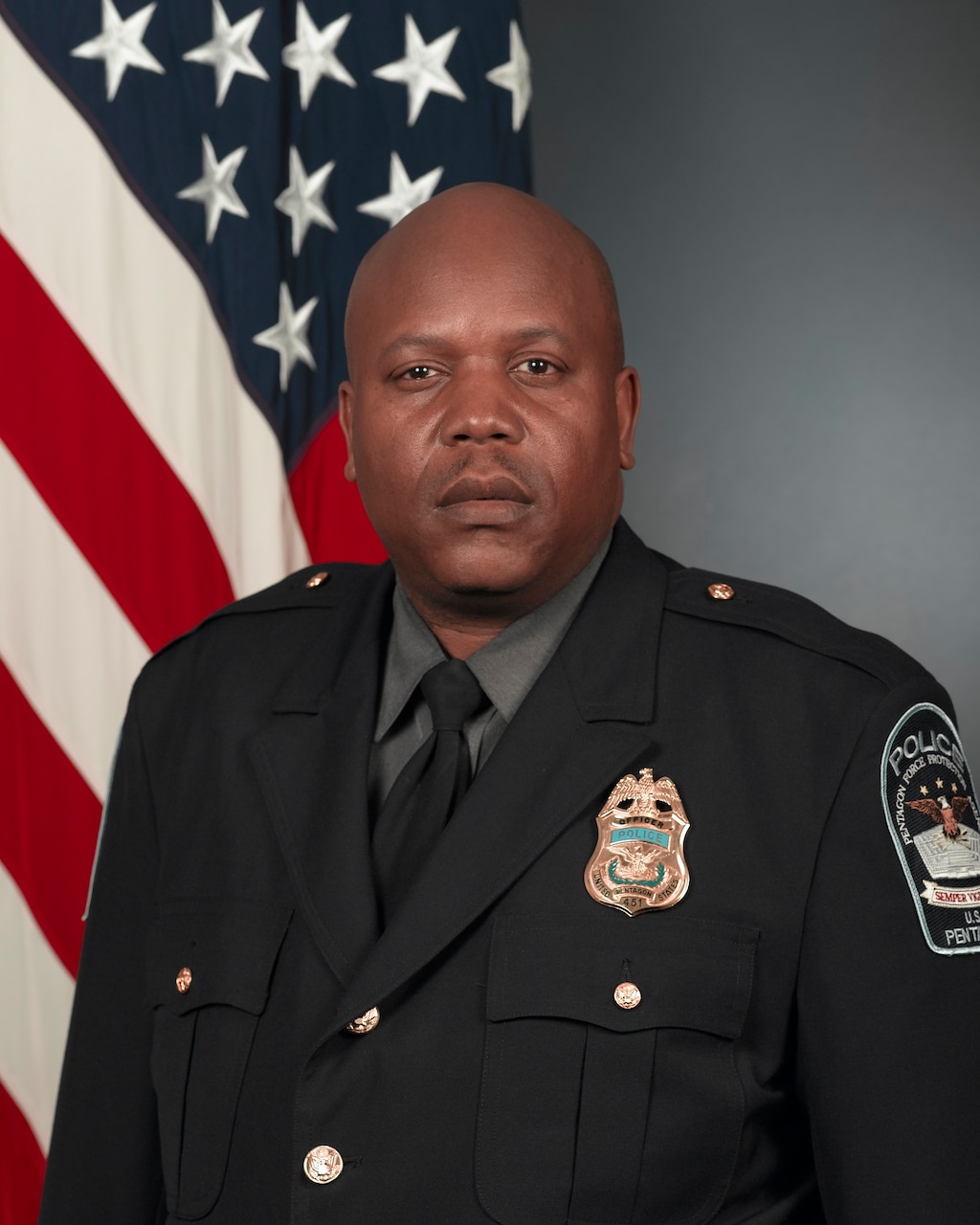 A man in a uniform poses for a photo in front of an American flag.