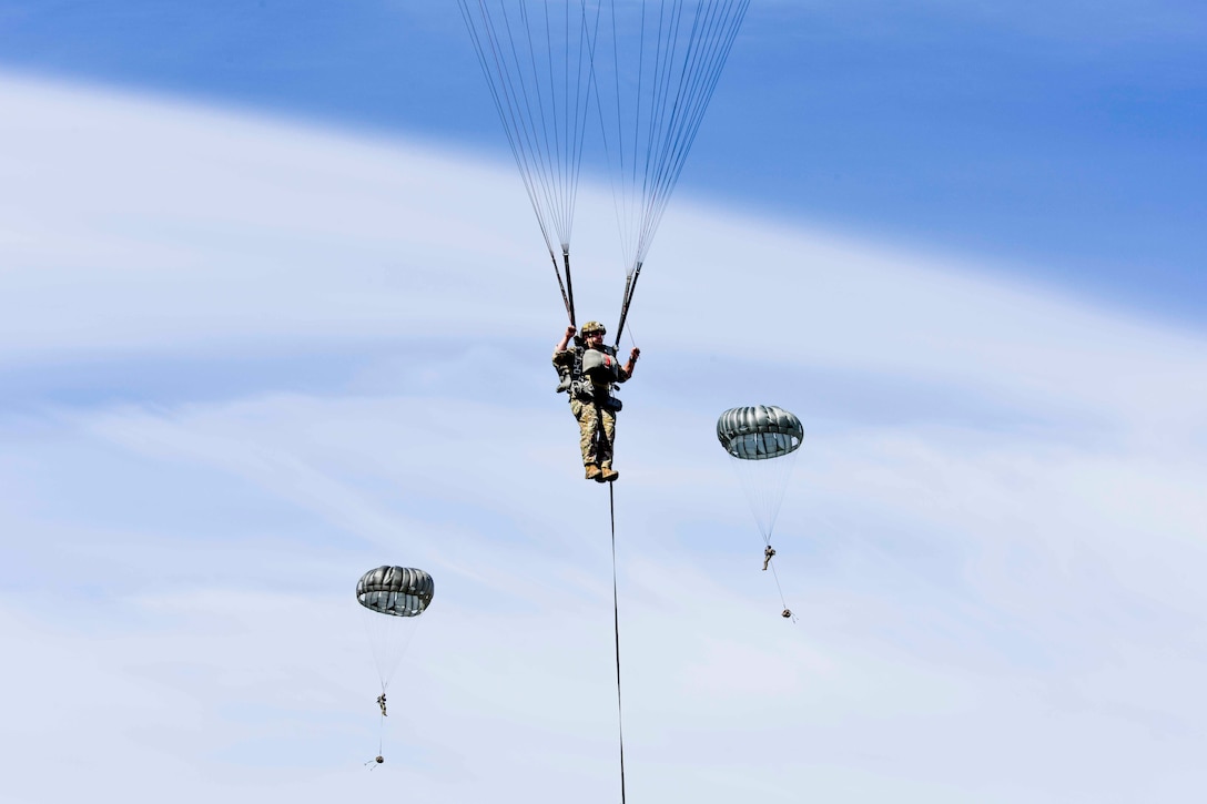 Three airmen descend in the sky wearing parachutes.
