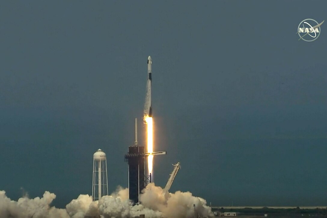 A rocket lifts off as a column of flames and smoke billow from beneath.