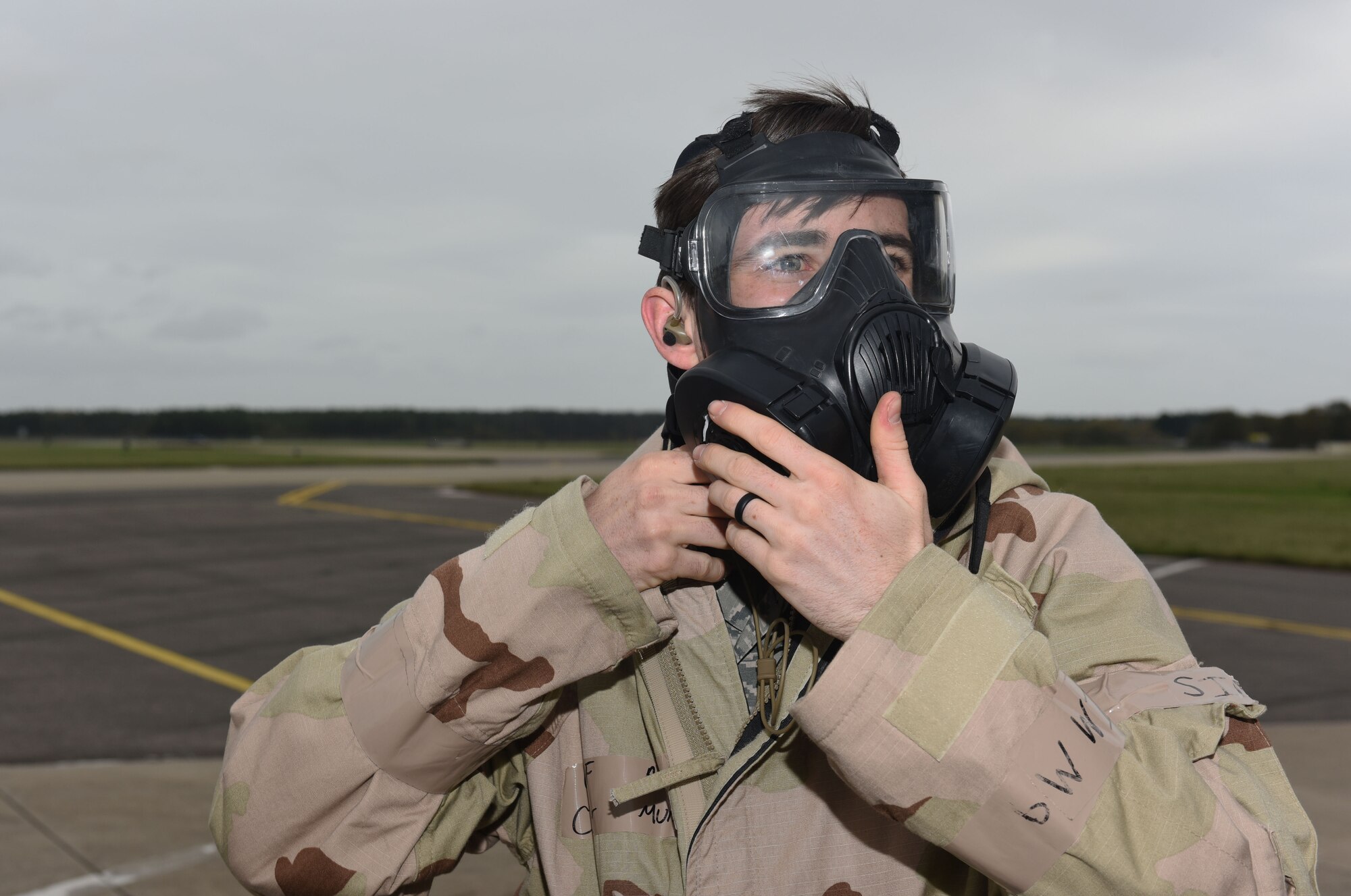 U.S. Air Force Airman 1st Class Cooper Murphy, 100th Aircraft Maintenance Squadron crew chief, puts on his gas mask after fitting an in-ear headset when an attack alarm is announced during a chemical, biological, radiological and nuclear exercise at Royal Air Force Mildenhall, England, Oct. 28, 2020. Mellott and another Airmen tested the innovative headset, which uses the bones in the user’s ear to transmit sound waves, to test its capabilities while being worn with mission-oriented protective posture gear ensuring they could communicate with aircrew while in the aircraft. (U.S. Air Force photo by Karen Abeyasekere)