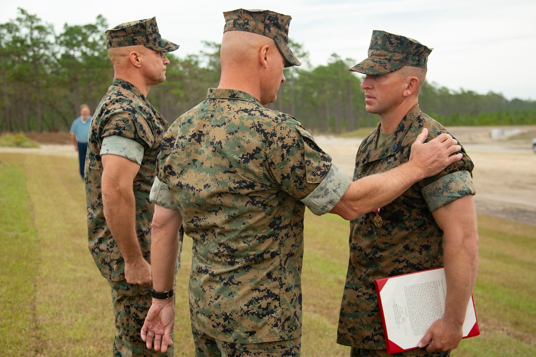 U.S. Marine Corps Maj. Gen. Julian D. Alford, center, commanding general, Marine Corps Installations East-Marine Corps Base Camp Lejeune, awards Gunnery Sgt. Jonathan E. Hill, right, heavy equipment chief with 2nd Combat Engineer Battalion, MCB Camp Lejeune, the Meritorious Achievement Medal on MCB Camp Lejeune, North Carolina, Oct. 29, 2020. Hill received the award for his efforts in building the G-36 Company Battle Course Range. G-36 has been redesigned to enable company commanders to train with organic weapons systems and attachments they would have available during combat and conduct full-scale operations on one range. (U.S. Marine Corps photo by Cpl. Ginnie Lee)