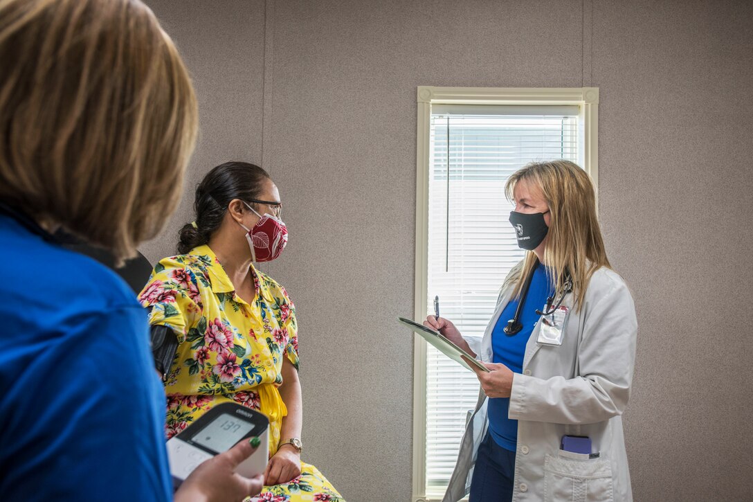 A woman wearing a face mask verifies a patient's health history.