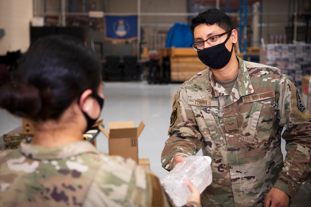 An airman wearing a face mask gives hand sanitizer to another airman.