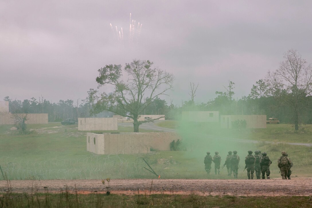 Soldiers carrying training rifles move towards a building covered by a green haze.