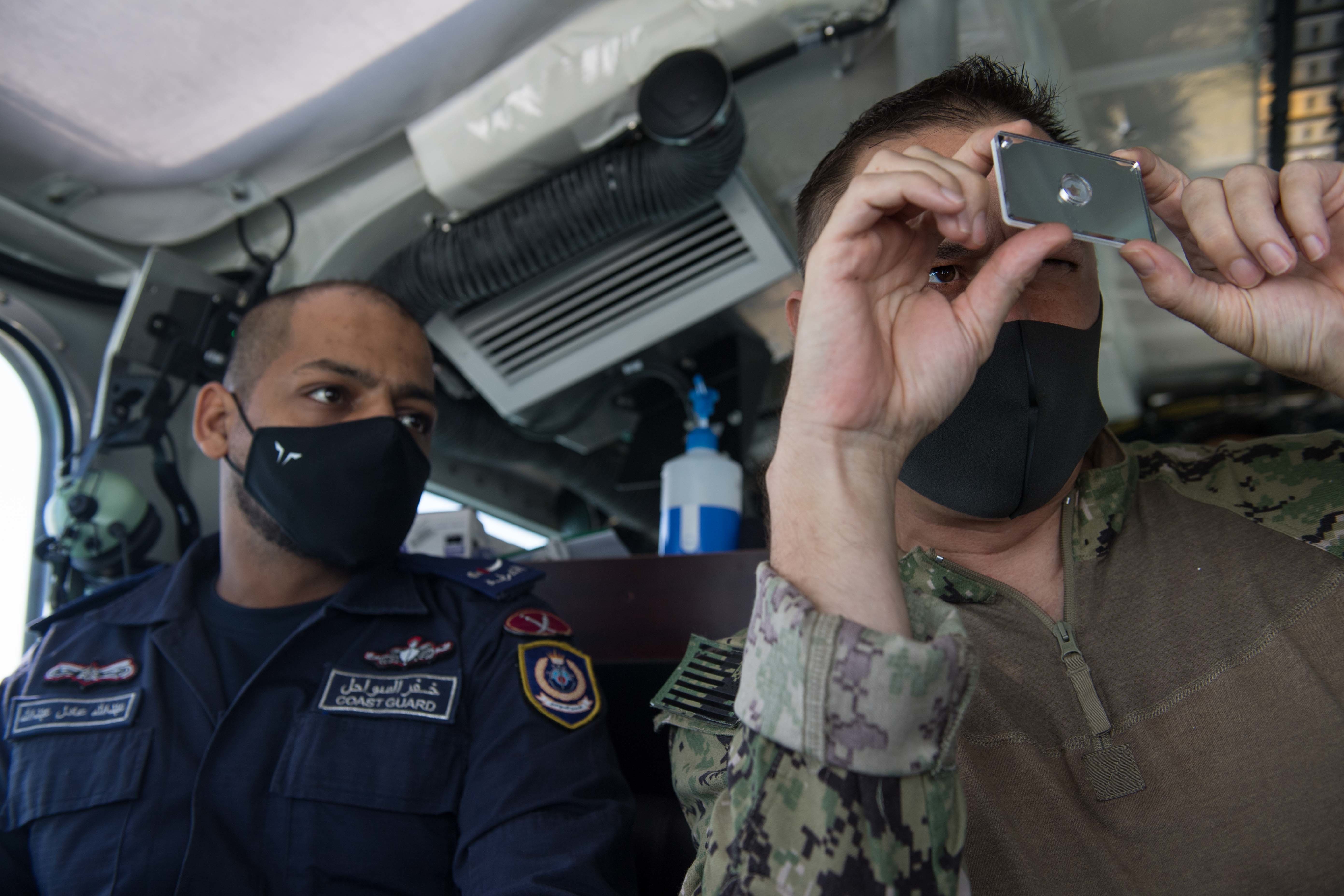 U.S. Coast Guard Boatswain's Mate 1st Class Shawn Wells, right, assigned to Patrol Forces Southwest Asia (PATFORSWA), shows Abdulla Alsaeed, a Bahrain Coast Guard coxswain, how to use a survival mirror aboard a Bahrain 45' Coast Guard response boat in the Arabian Gulf.