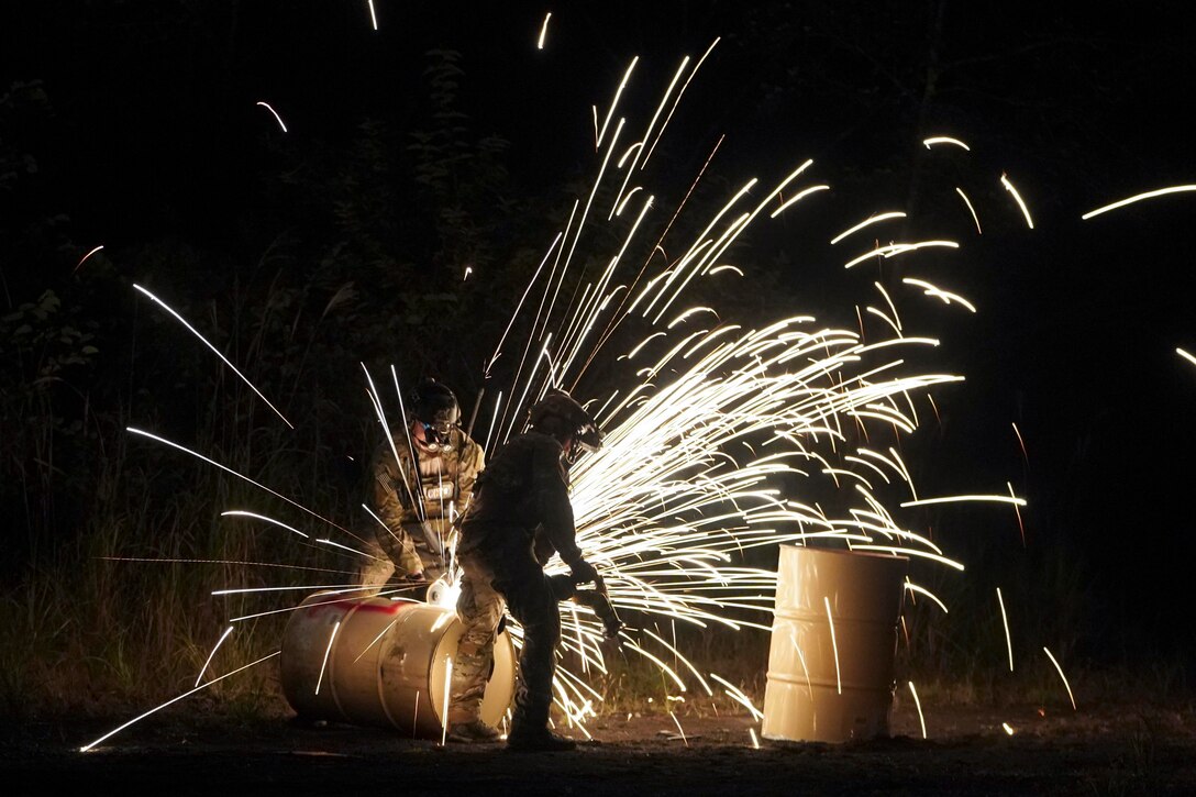 Airmen cut into barrels causing sparks to fly.