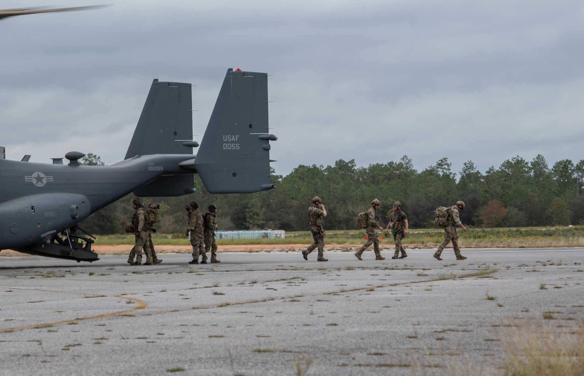 We see the tail of a dual-rotor helicopter parked off-camera to the left of the picture. A team of Special Tactics operators is walking away from the ramp to the right carrying equipment.