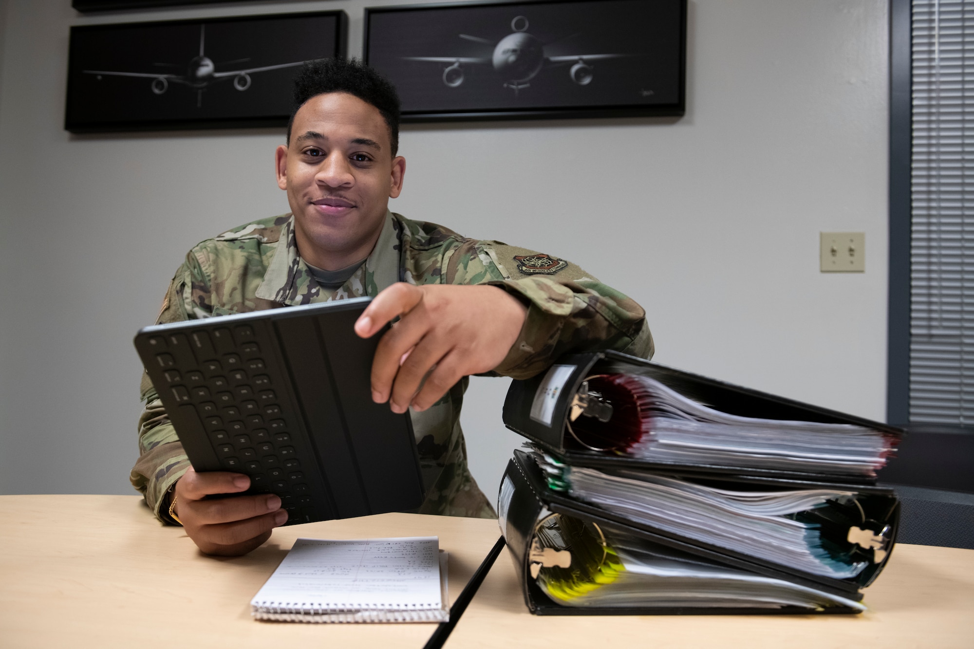 U.S. Air Force Senior Airman Isaiah Hammond, 60th Air Mobility Wing Command Post emergency actions controller, poses for a photo while sitting at a desk carrying an electronic tablet Sept. 17, 2020, at Travis Air Force Base, California.