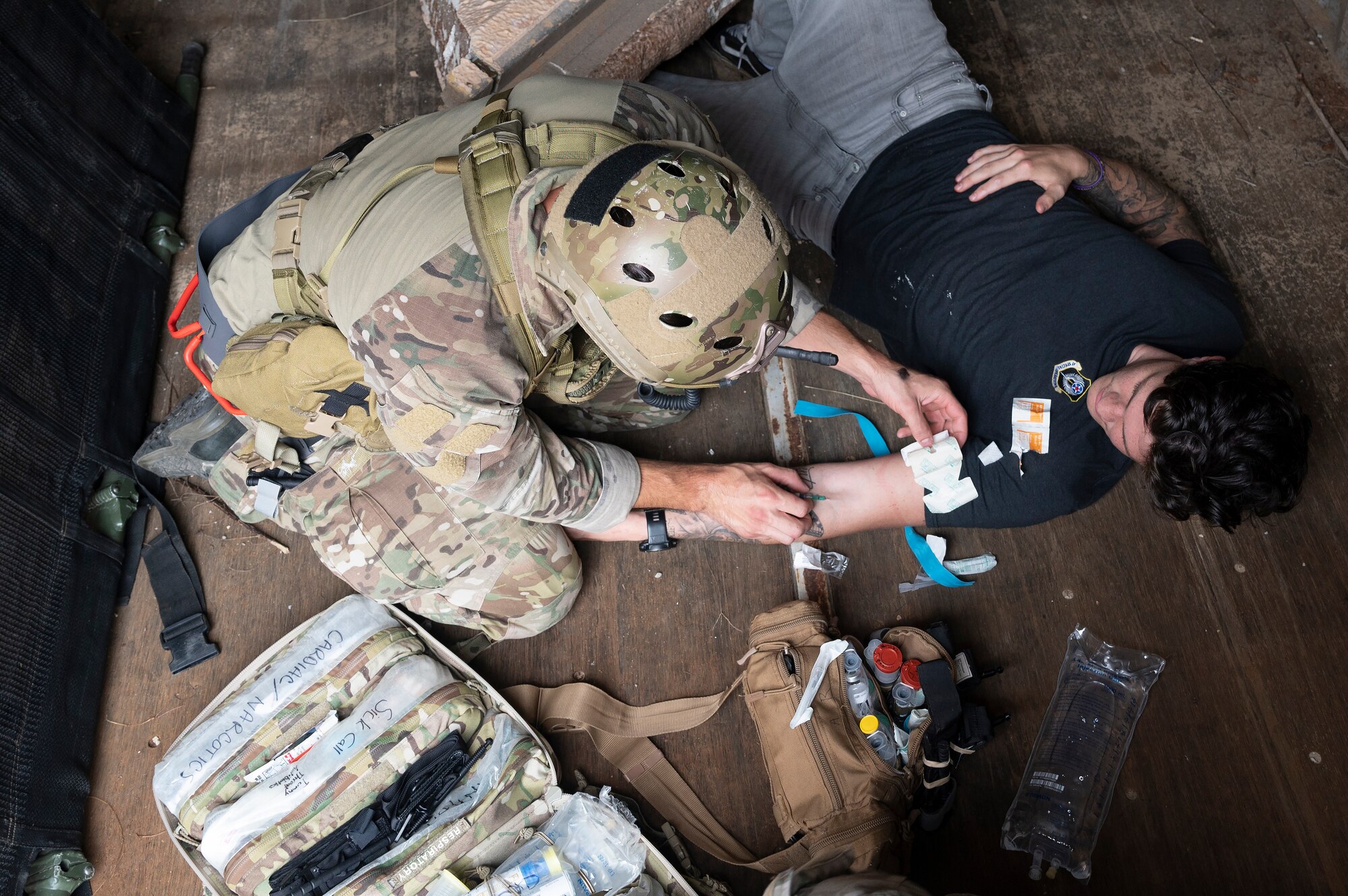 We look down from above at a Special Tactics Operator applying a dressing to a victim's left arm during training.