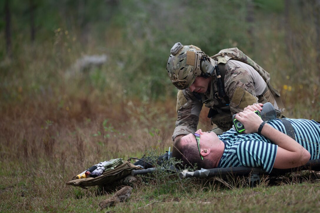 A Special Tactics Operator kneels on the far side of a patient in a stretcher during training.