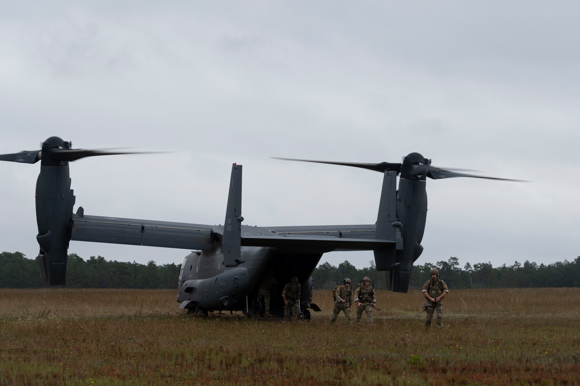 Three Special Tactics operators have just walked off of the ramp of a dual-rotor helicopter in the middle of a field.