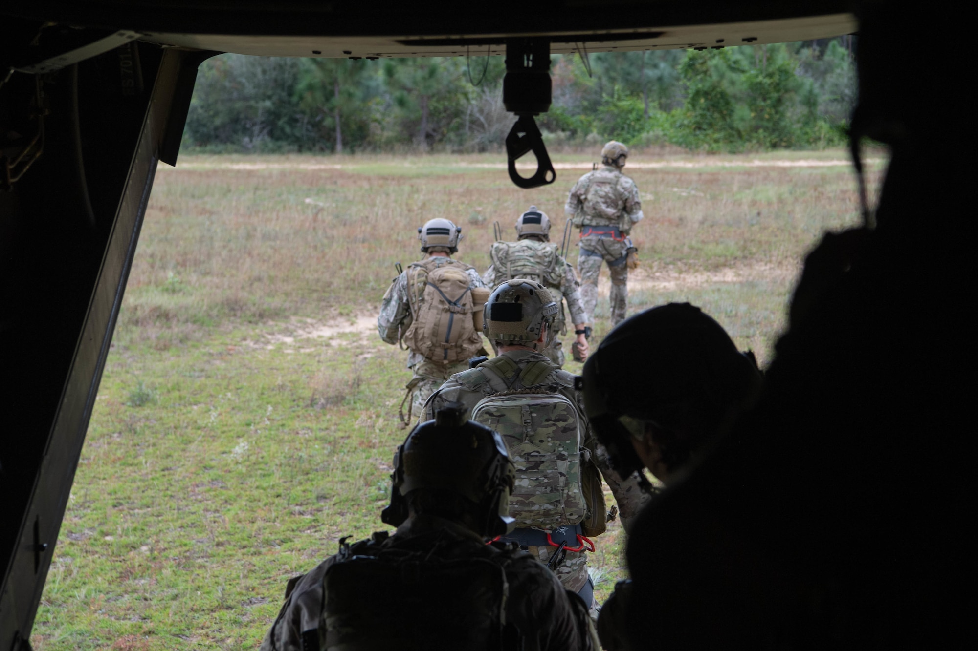 We look out the ramp of a helicopter on the ground as a line of Special Tactics operators disembark and walk away from the helicopter.