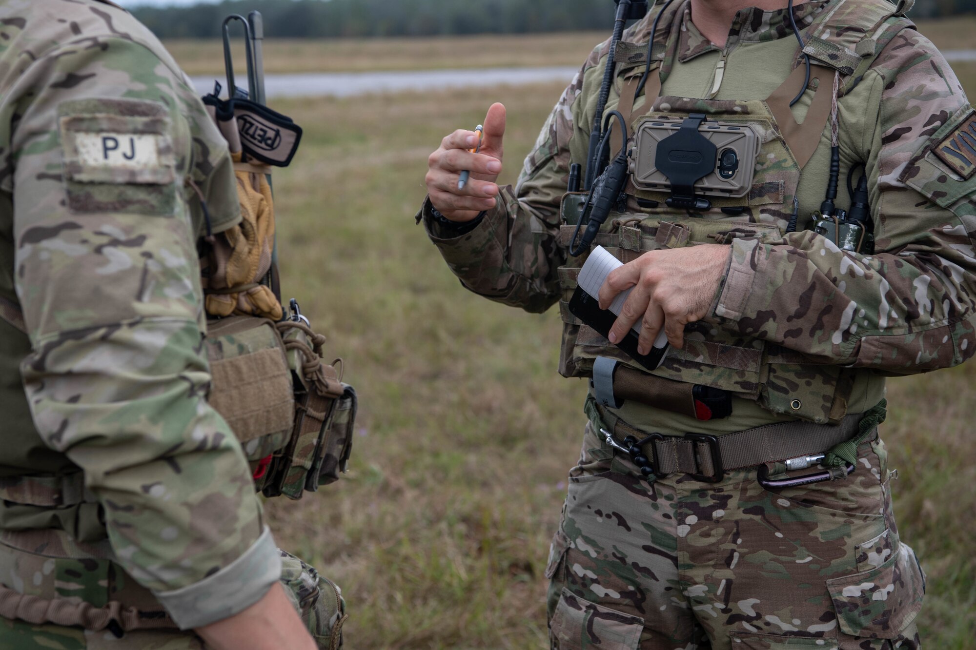 From the side we see the torsos of two Special Tactics operators as they exchange information. The operator on the right is using his hands to make a point as he talks. We can see the "PJ" shoulder patch insignia on the operator on the left indicating that he is a "pararescue jumper."