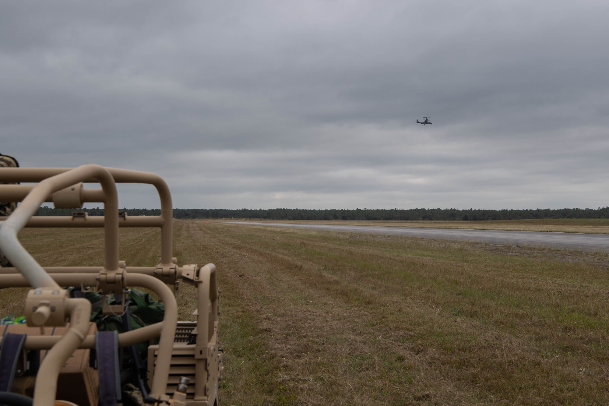 Far off in the distance, a dual-rotor helicopter approaches a road that the Special Tactics operators are using as a landing zone. We can see some equipment sitting close to us as we look across the field at the helicopter.