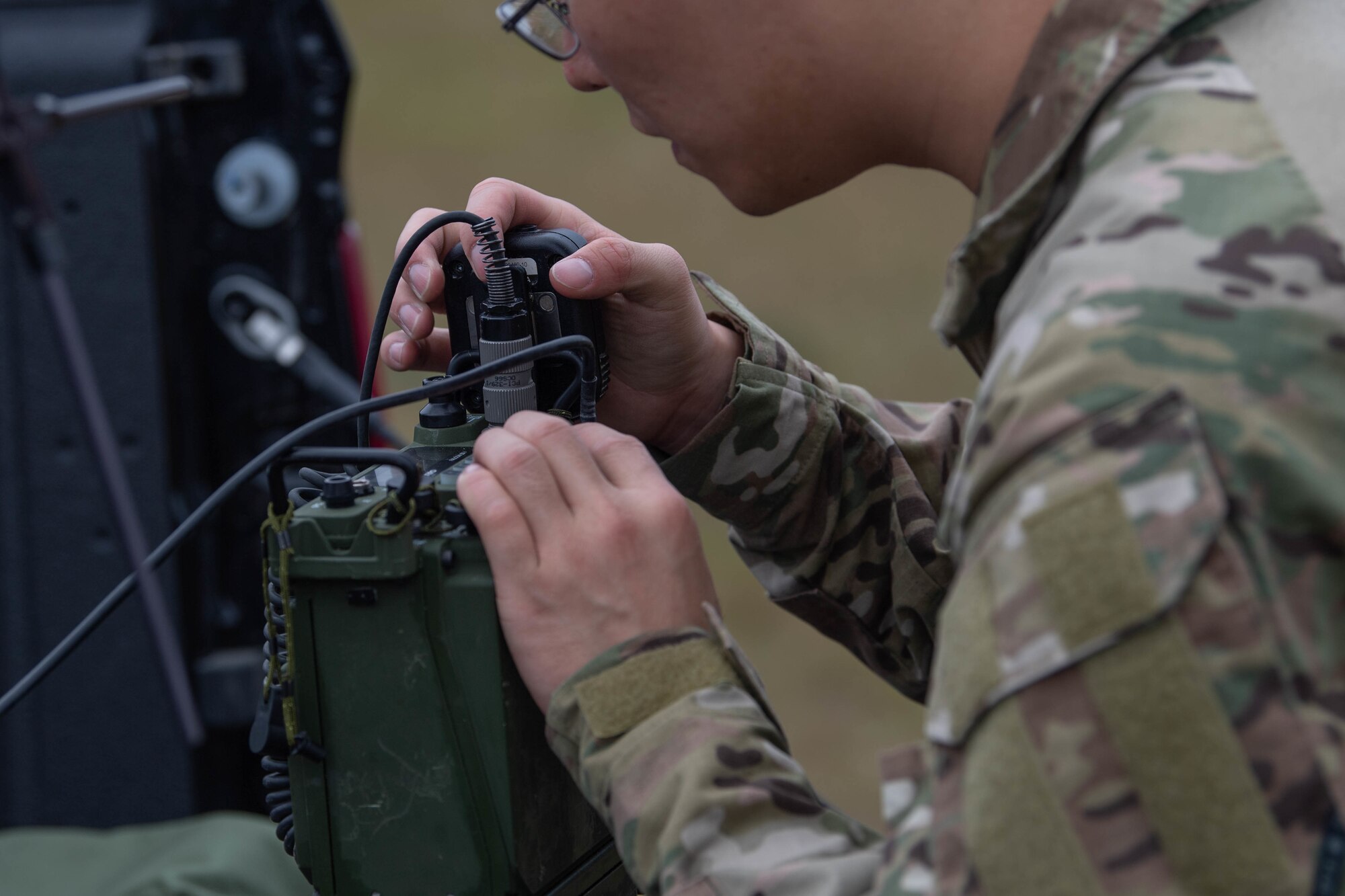 A Special Tactics operator wearing glasses works on black boxes containing radio gear. The operator is working to connect the boxes together so operators can talk to one another during the emergency response.