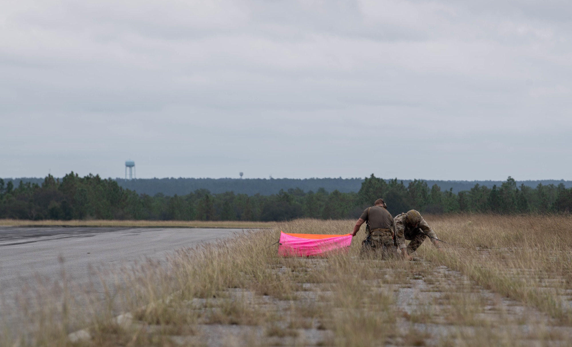 Two Special Tactics operators set up a bright pink panel beside the road in the distance to help aircraft locate the landing area.