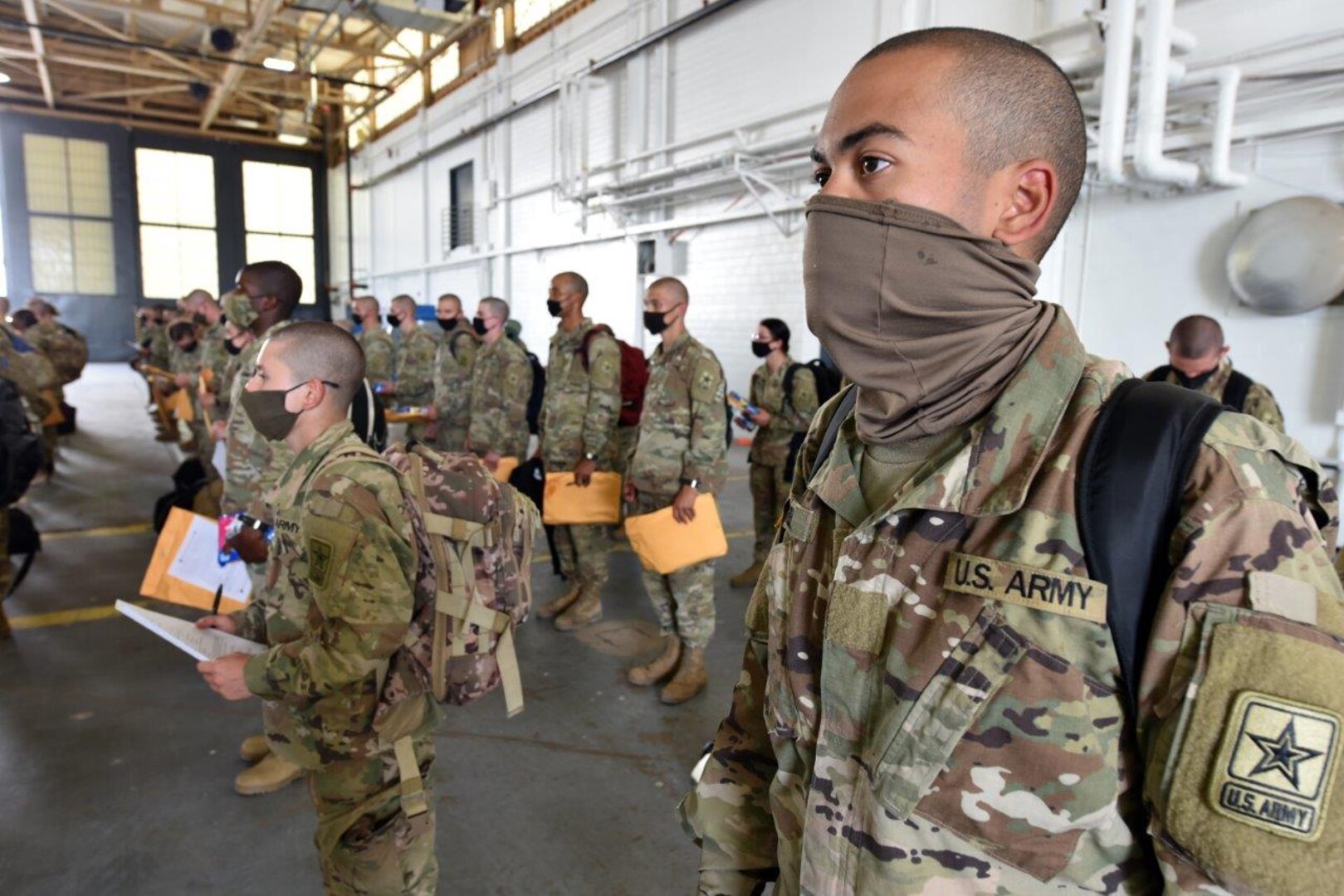 Soldiers stand in formation inside a hangar at Joint Base San Antonio-Kelly Field Annex during a layover as they travelled from Fort Jackson, Mississippi, to Fort Huachuca, Arizona. They were on a chartered flight along with Soldiers that also departed Fort Jackson to begin training at the U.S. Army Medical Center of Excellence.