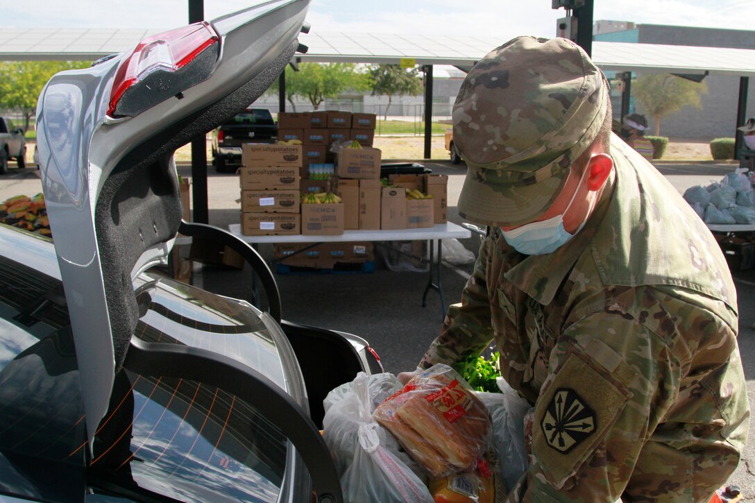 A national guardsman wearing a face mask puts groceries into a vehicle.