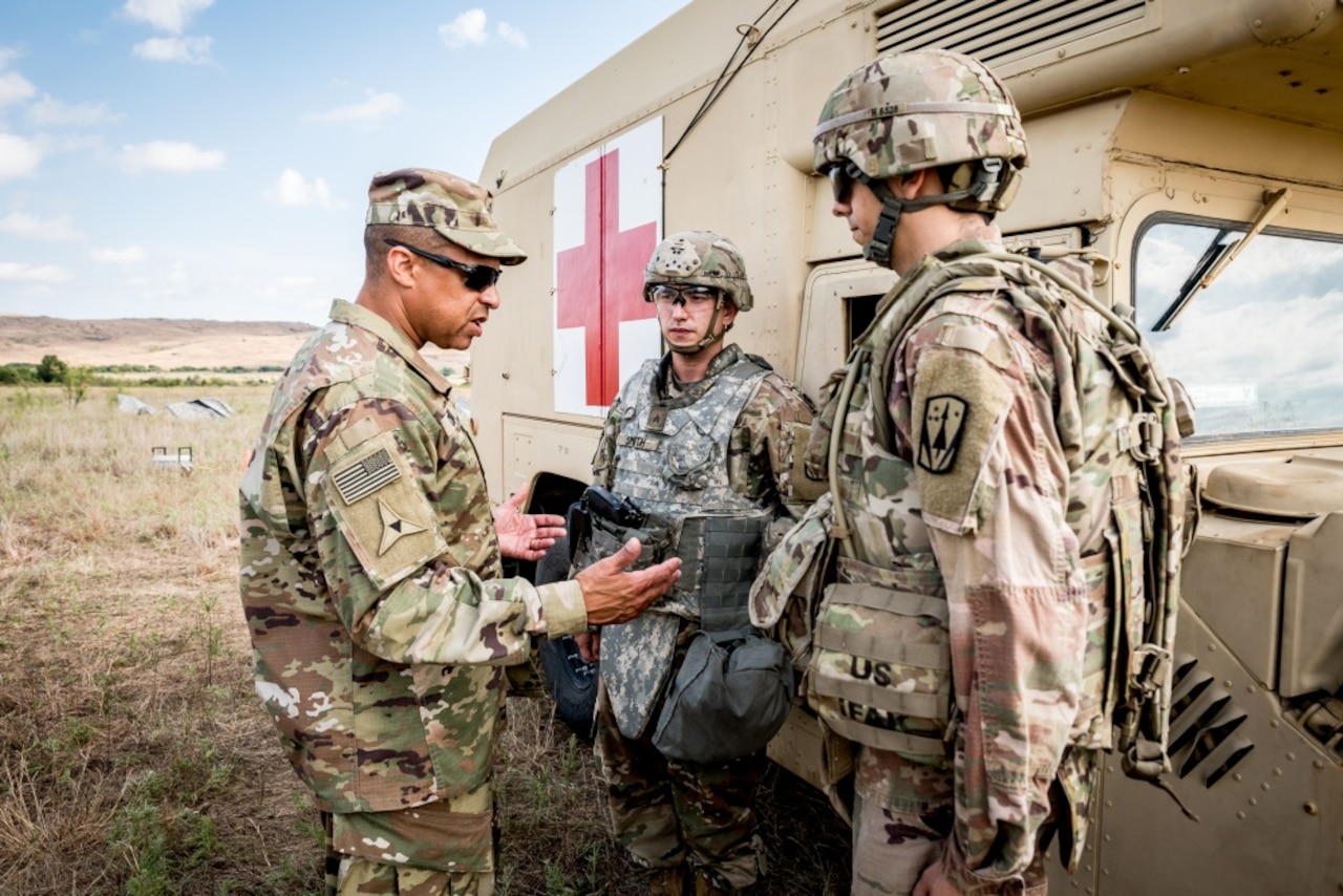 Three men stand beside a large vehicle bearing a red cross and talk.