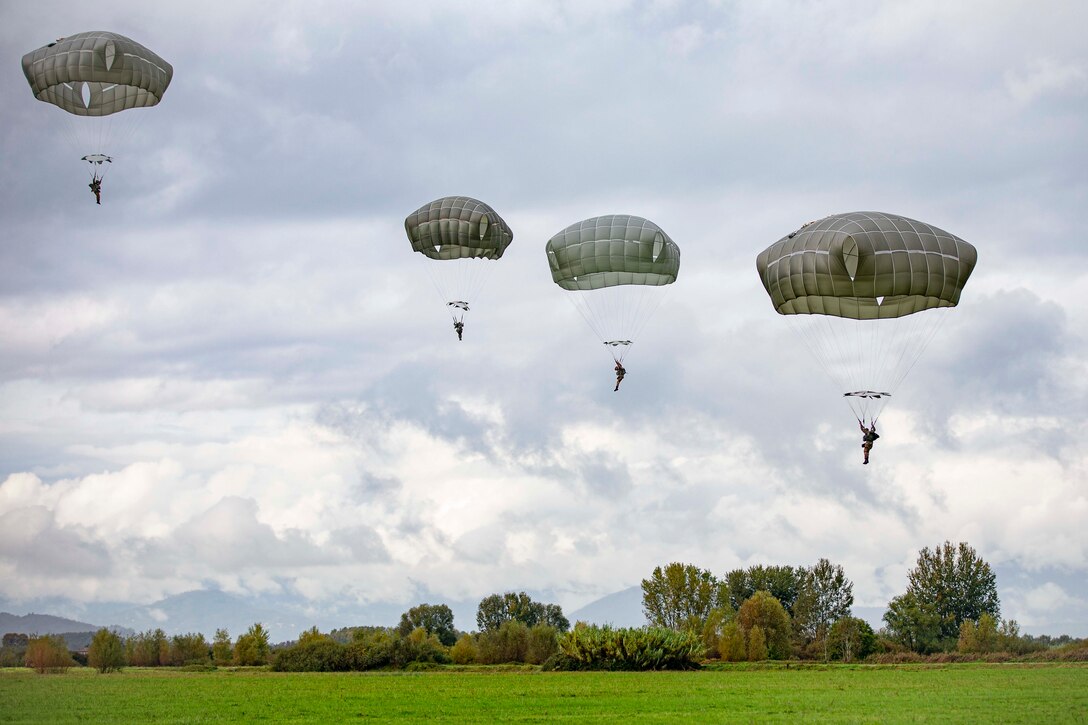 Four soldiers descend in the sky wearing parachutes.