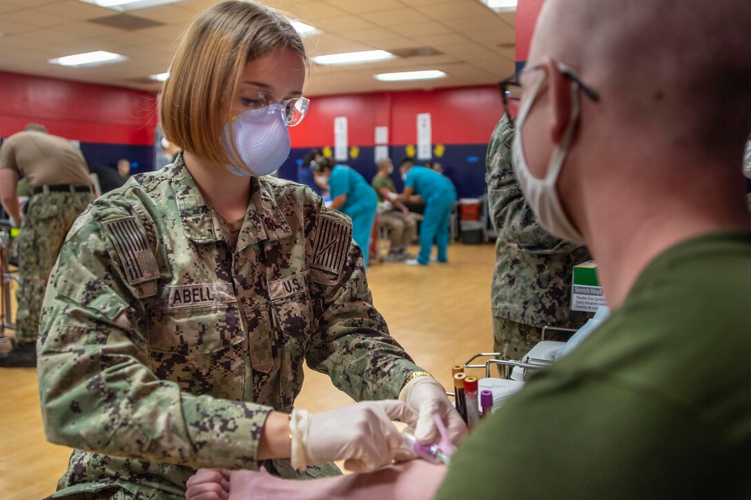 A female sailor draws blood from a recruit.