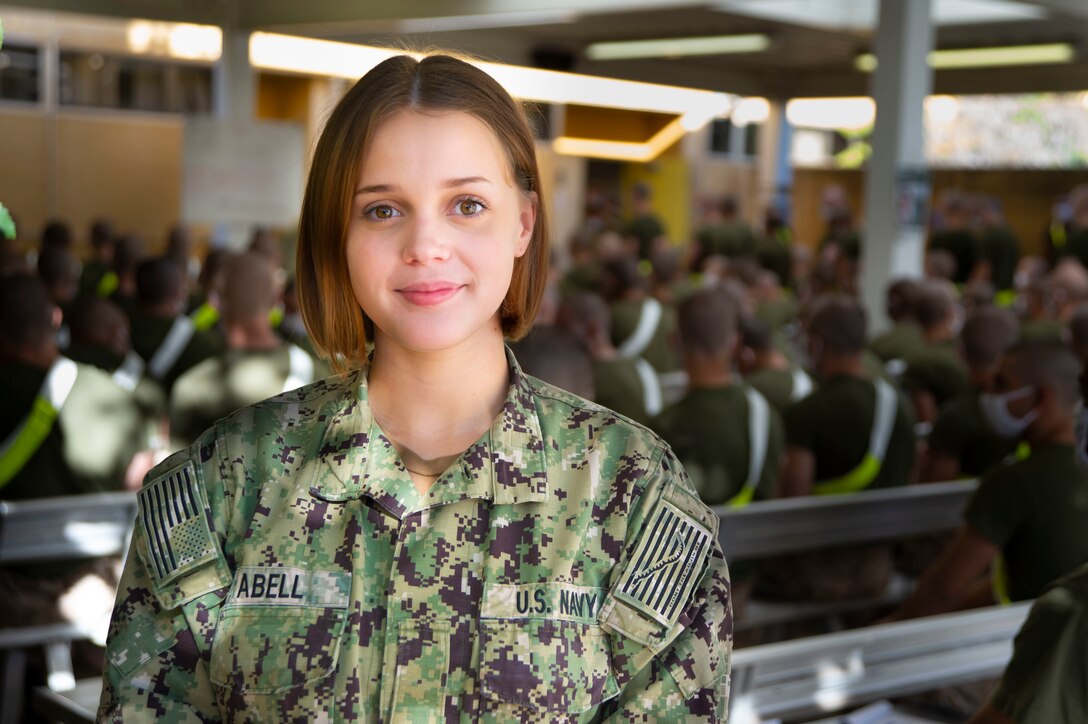 A female sailor poses for a photograph in front of Marine recruits.