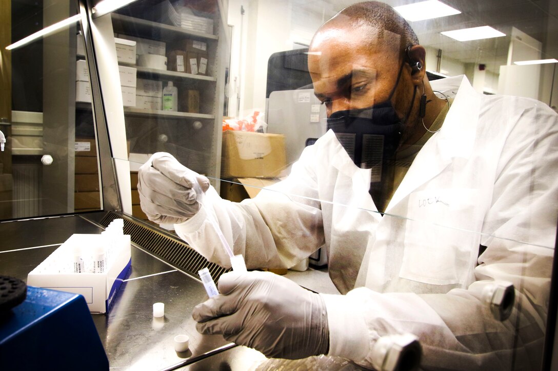 A soldier wearing personal protective equipment prepares a COVID-19 sample for testing