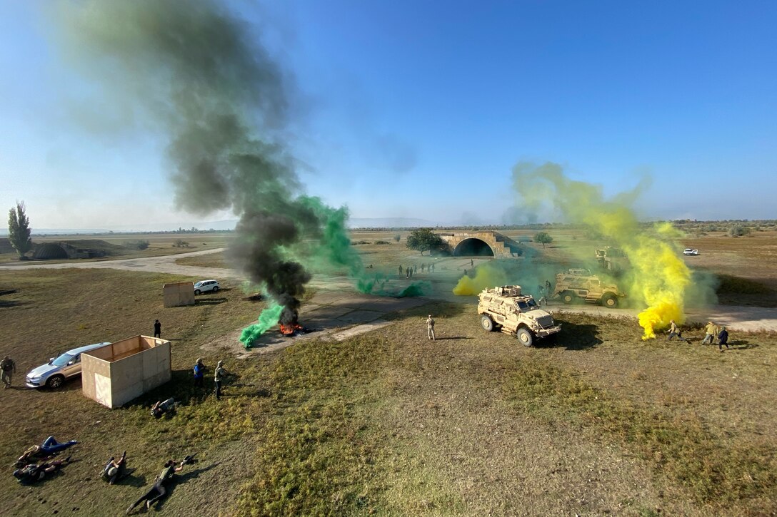 Green and yellow smoke rises up from a large field of dirt.