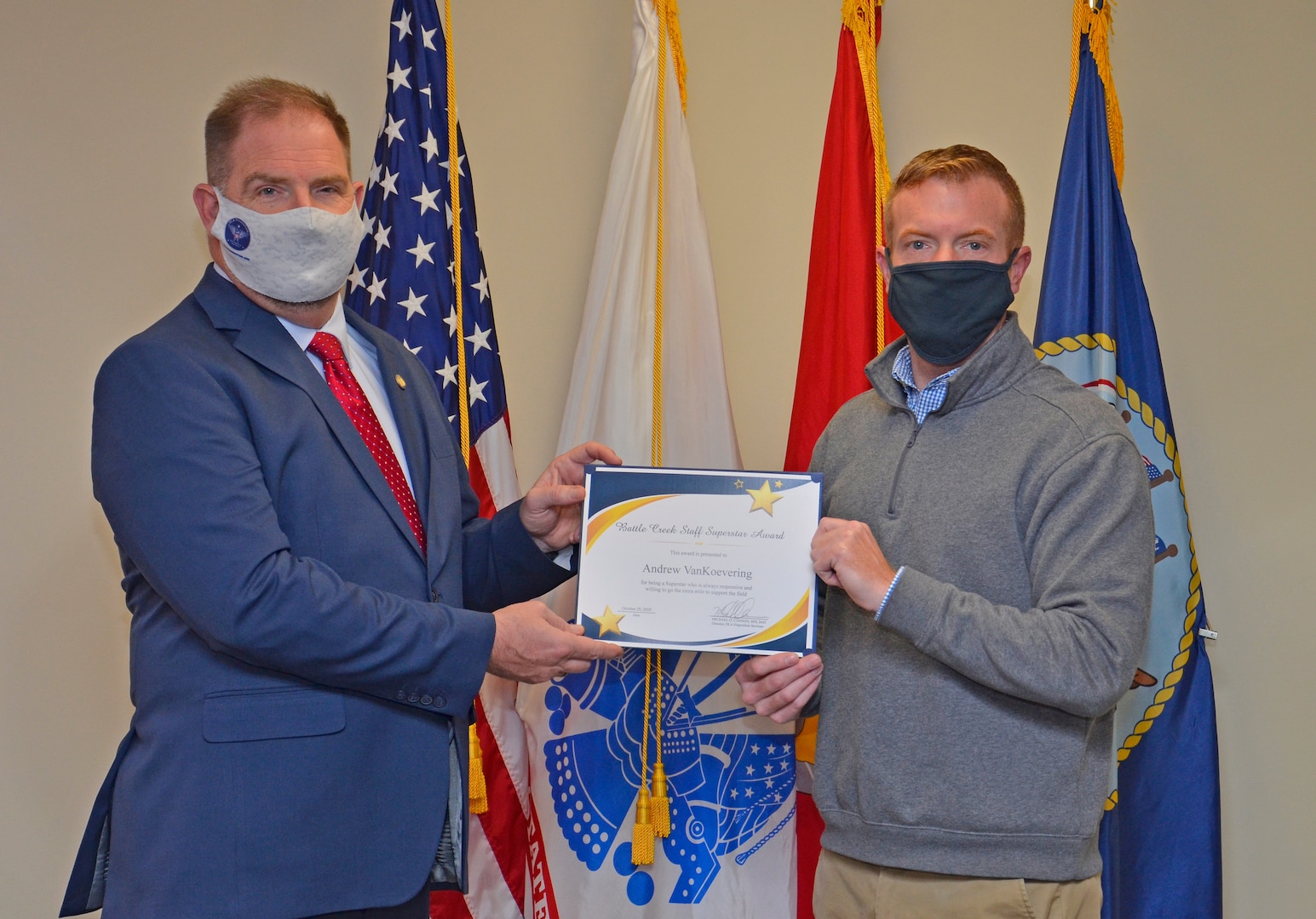 Command director congratulates employee in front of a flag.