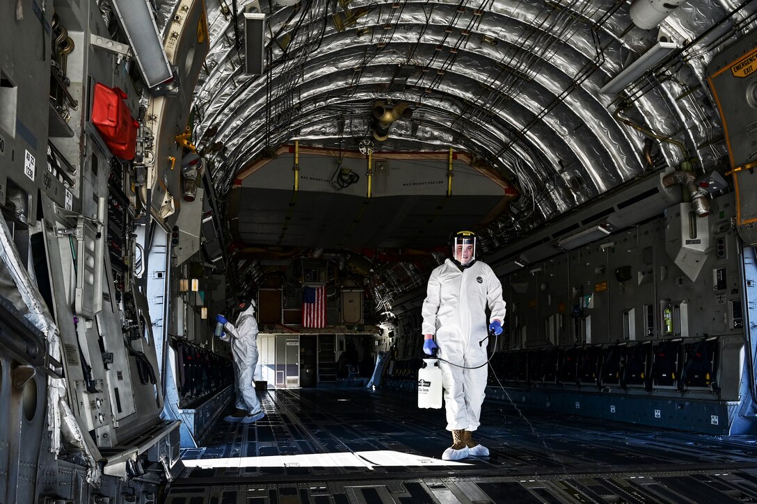 Airmen wearing personal protective equipment clean the inside of a C-17 Globemaster III.
