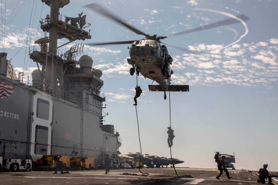 Marines rappel from a helicopter hovering over a ship.