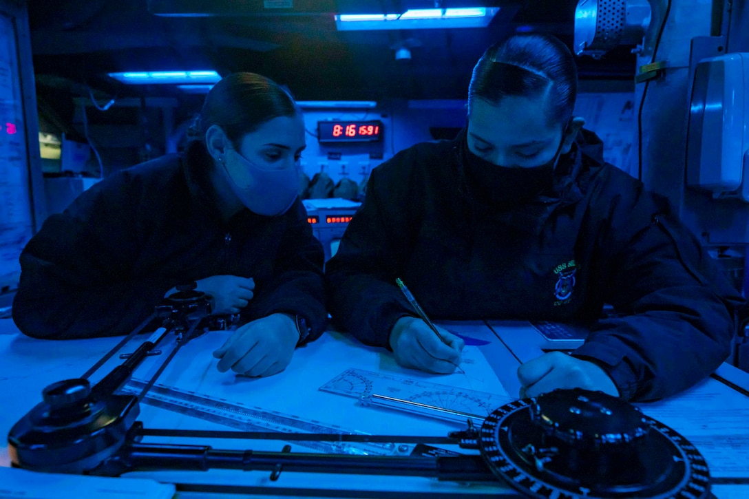 Two sailors illuminated by blue light work at a desk.