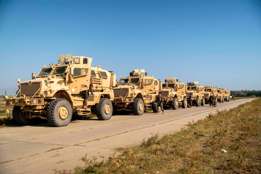 Marines walk beside a line of military vehicles.