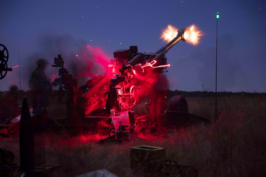 Soldiers fire an M777 howitzer at night.