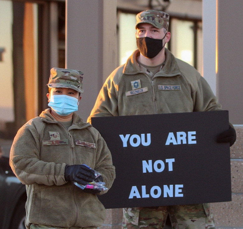 Master Sgt. Mercylen Ayo, 21st Medical Squadron superintendent, left, prepares to hand out candy to Airmen and civilians at the North gate while Chief Master Sgt. Michael Rozneck, Delta 8 senior enlisted leader, holds a sign during the Don’t Give Up event at Schriever Air Force Base, Colorado. Thirteen Airmen greeted fellow Wingmen for more than two hours at the gate. (U.S. Space Force photo by Marcus Hill)