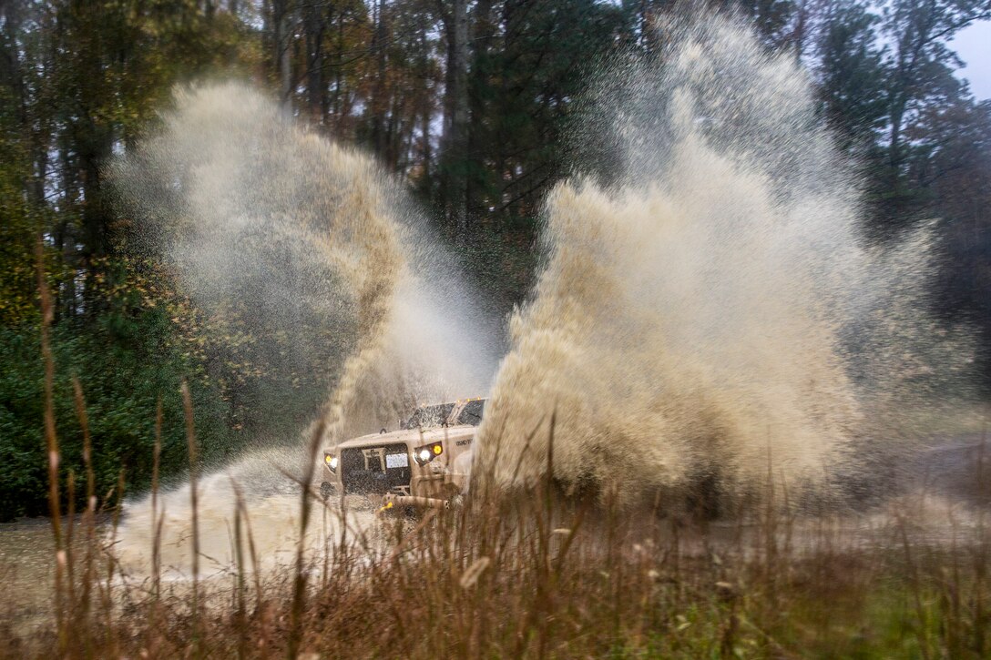 A Marine Corps vehicle creates a huge splash as it drives through muddy water.