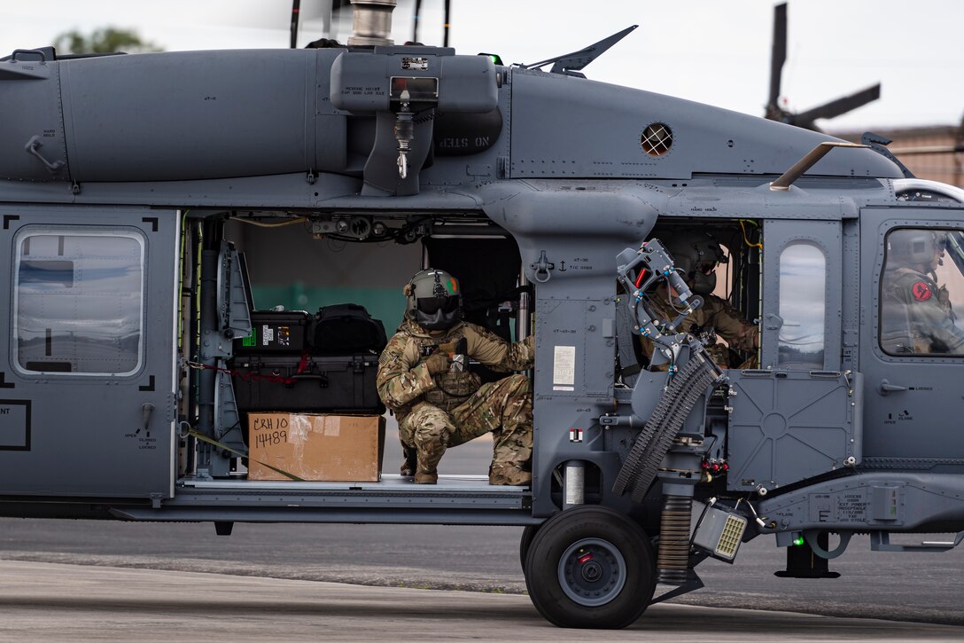 A photo of an Airman looking out of a helicopter