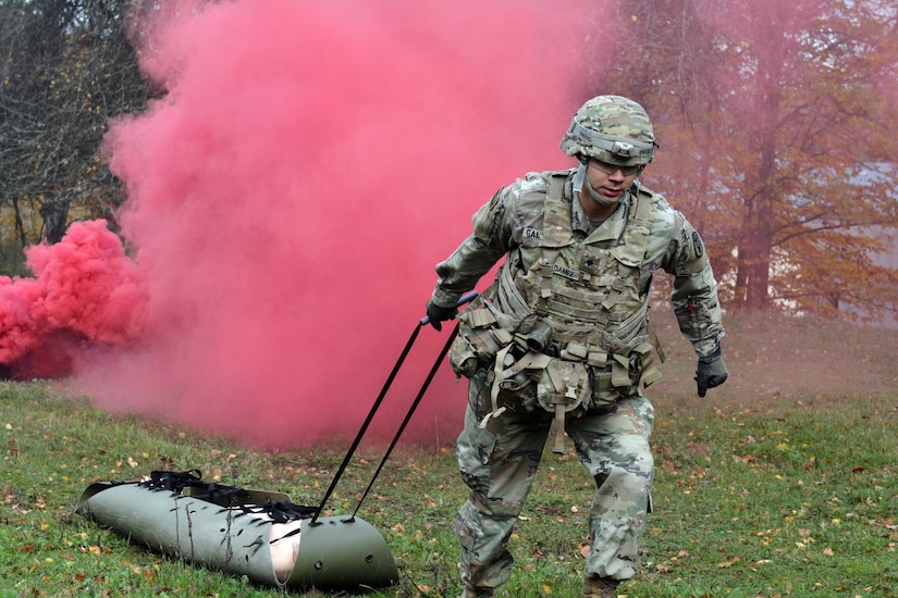 A soldier drags a stretcher away from a plume of pink smoke.
