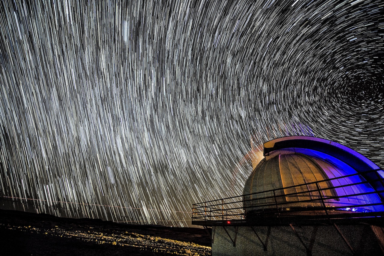 Curved lines of light fill a night sky above a planetarium-like structure.