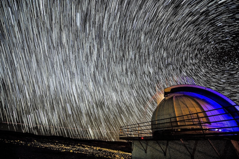 Curved lines of light fill a night sky above a planetarium-like structure.