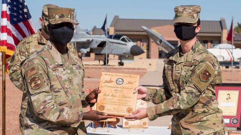 Senior Airman Ayla Squires, right, Airman Leadership School graduate, accepts the distinguished graduate award during the graduation of ALS class 21-1, Nov. 5, 2020, on Holloman Air Force Base, New Mexico. The distinguished graduate award is presented to the top ten-percent of graduates for their performance in academic evaluations and demonstration of leadership. (U.S. Air Force photo by Staff Sgt. Christine Groening)