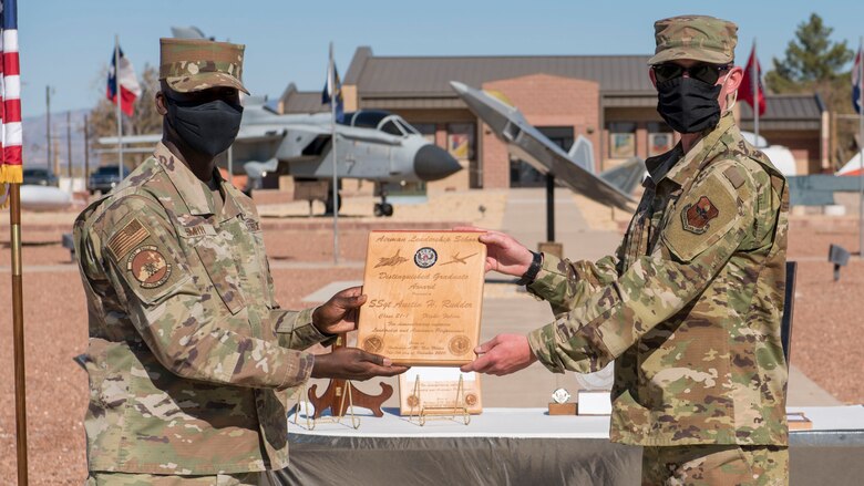 Staff Sgt. Austin Rudder, right, Airman Leadership School graduate, accepts the distinguished graduate award during the graduation of ALS class 21-1, Nov. 5, 2020, on Holloman Air Force Base, New Mexico. The distinguished graduate award is presented to the top ten-percent of graduates for their performance in academic evaluations and demonstration of leadership. (U.S. Air Force photo by Staff Sgt. Christine Groening)